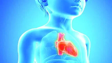 A young child holding a heart-shaped pillow, symbolizing awareness of heart problems in children.