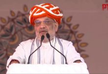 બનાસ ડેરીના સણાદર પ્લાન્ટ ખાતે કેન્દ્રીય ગૃહ અને સહકાર પ્રધાન અમિત શાહ વિવિધ પ્રકલ્પોના લોકાર્પણ અને મુલાકાત દરમિયાન, પાછળ બનાસ ડેરીનો લોગો અને ભીડ દેખાય છે.